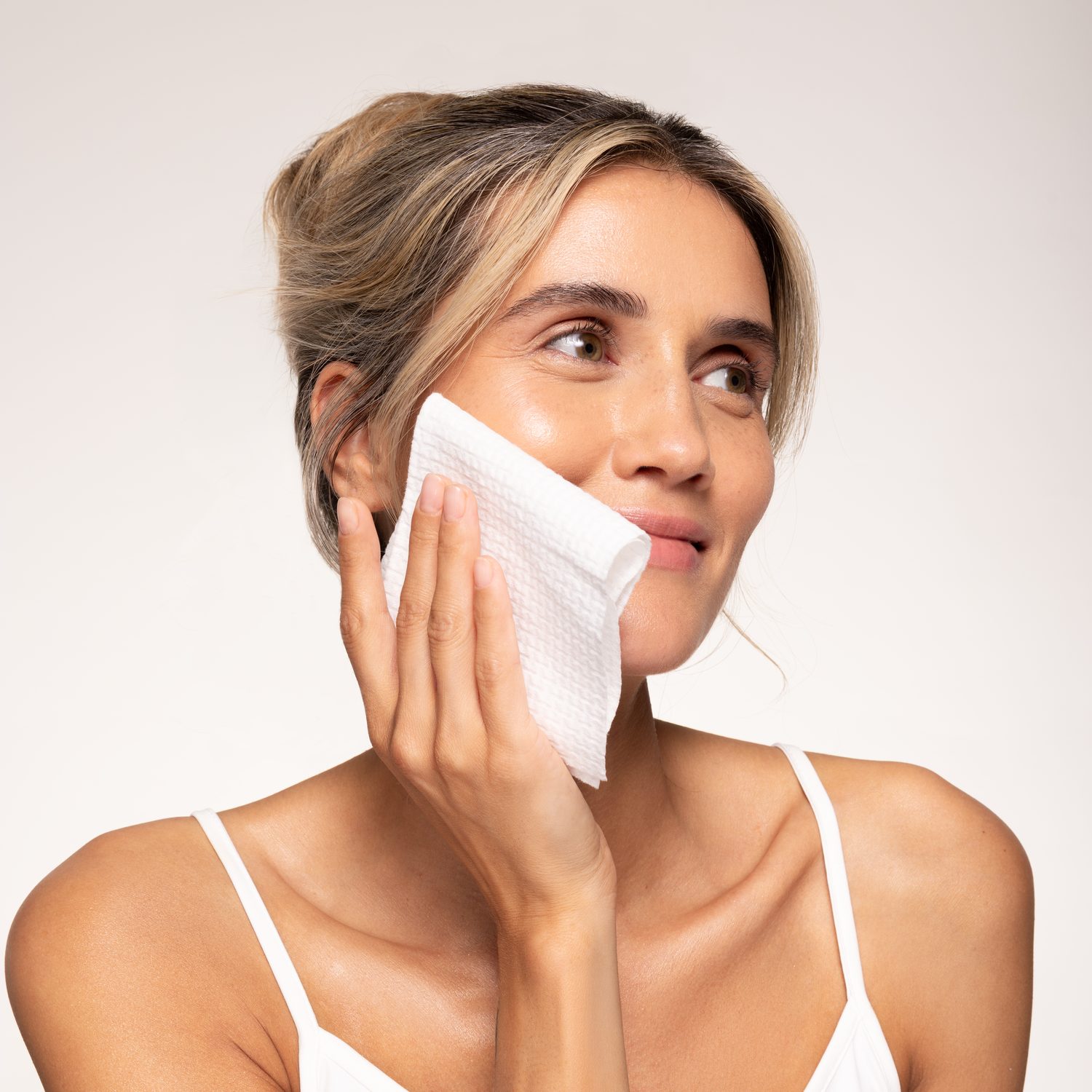 Uśmiechnięta kobieta delikatnie przykłada do policzka miękki, jednorazowy ręcznik do twarzy Pure Face Towels